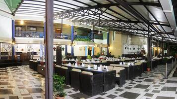 A spacious indoor dining area with multiple levels, featuring a checkered floor, wicker furniture, and a covered upper level with a balcony.