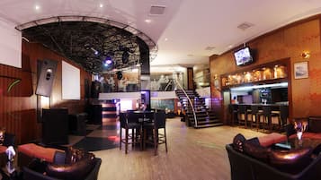 Un área de bar o salón con un escenario, asientos y una escalera que conduce a un nivel superior.