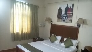 A hotel room with a large bed, two bedside tables, a nightstand, a lamp, a painting on the wall, and a window with curtains. - La Ben Resort (Colva)