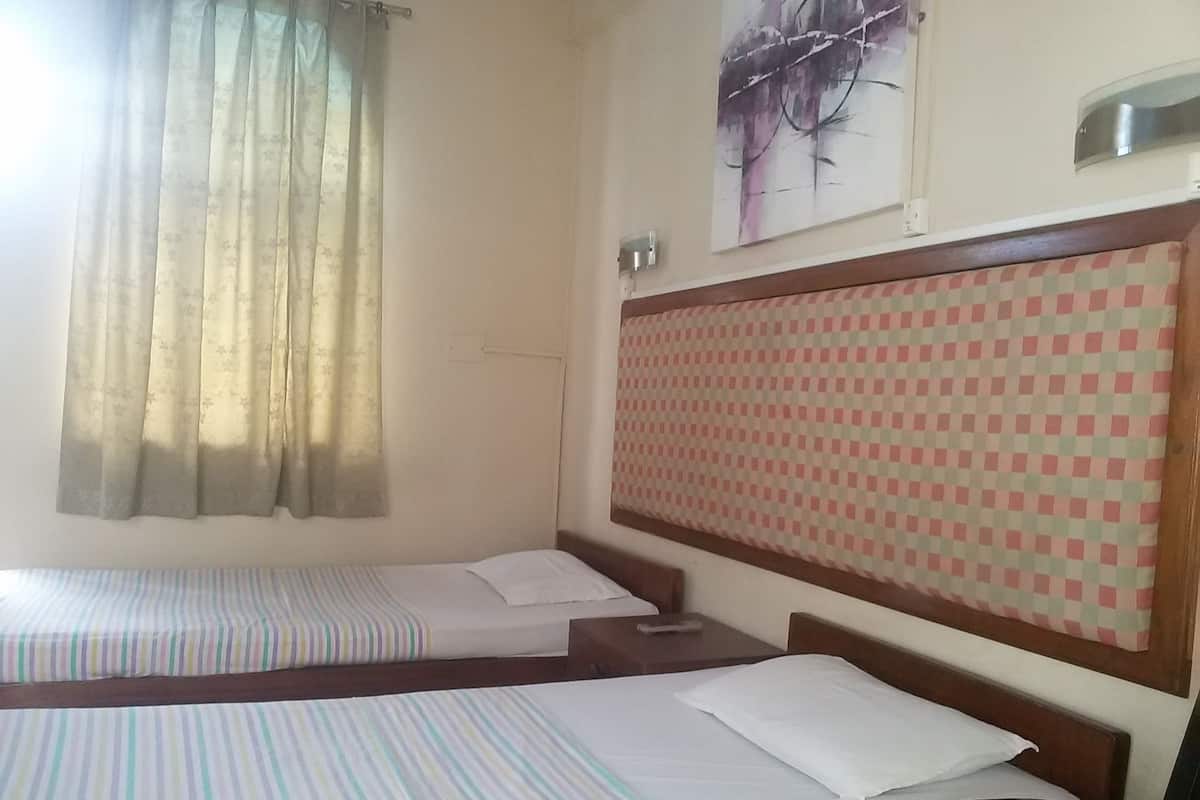 A hotel room with two single beds, a checkered headboard, a painting on the wall, and a window with curtains.