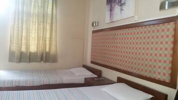Habitación de hotel con dos camas individuales, cabecera a cuadros, un cuadro en la pared y una ventana con cortinas.