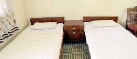 A room with two single beds, a wooden nightstand with drawers, and a patterned rug.