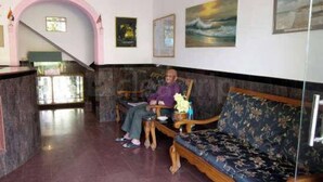 A man sitting on a wooden bench in a lobby with a marble floor, a staircase, and framed artwork on the walls. - La Ben Resort (Colva)