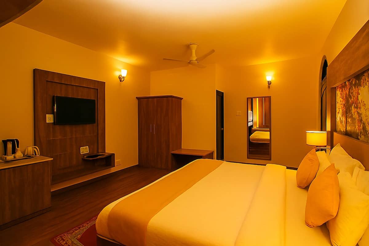 A hotel room with a bed, a flat-screen TV, a wardrobe, a desk with a lamp, and a ceiling fan.