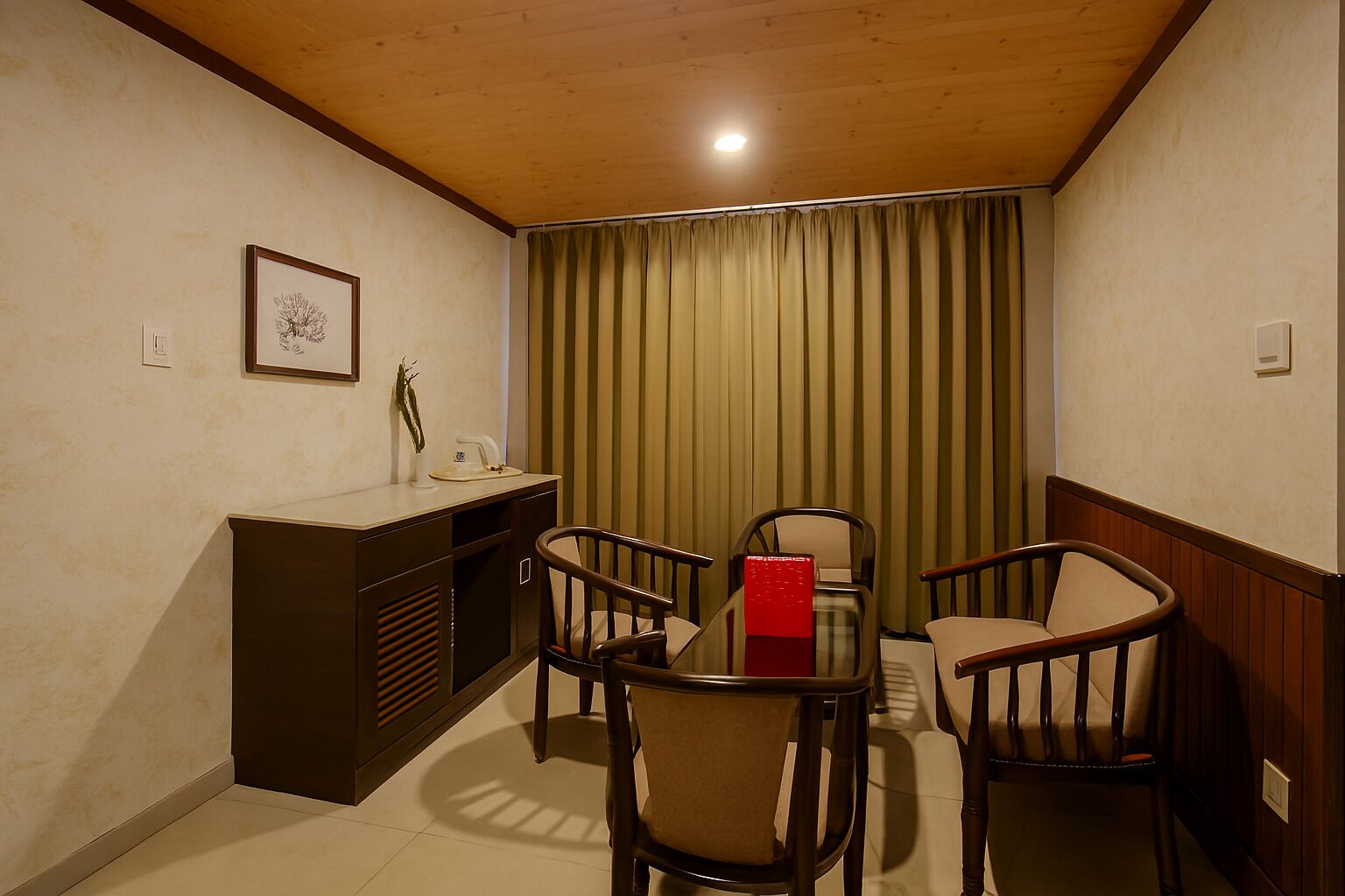Une petite pièce agréable, avec un plafond en bois, un bureau agrémenté d’une plante, deux chaises et un rideau vert.