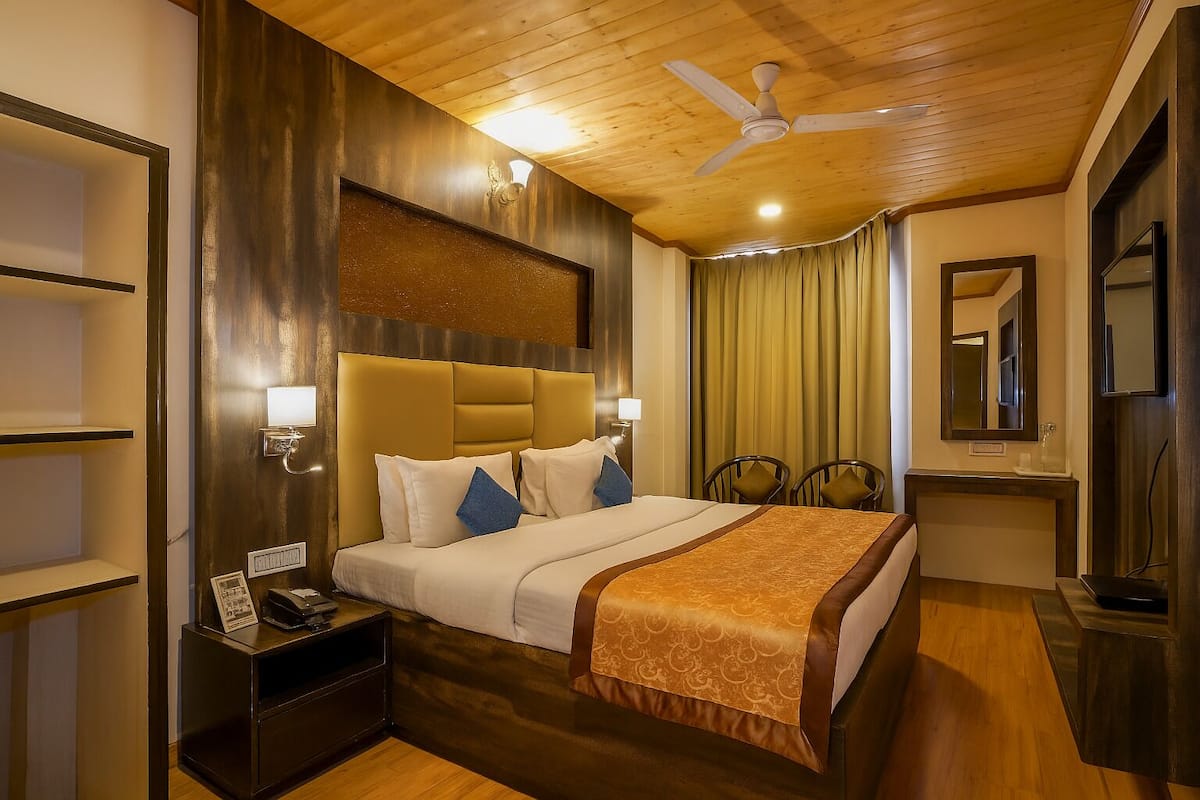 A hotel room with a wooden ceiling, a large bed with a headboard, bedside lamps, a nightstand, a mirror, and a window with curtains.