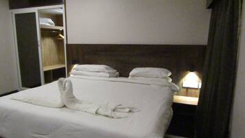 A hotel room with a neatly made bed, a wardrobe, and a bedside table with a lamp.