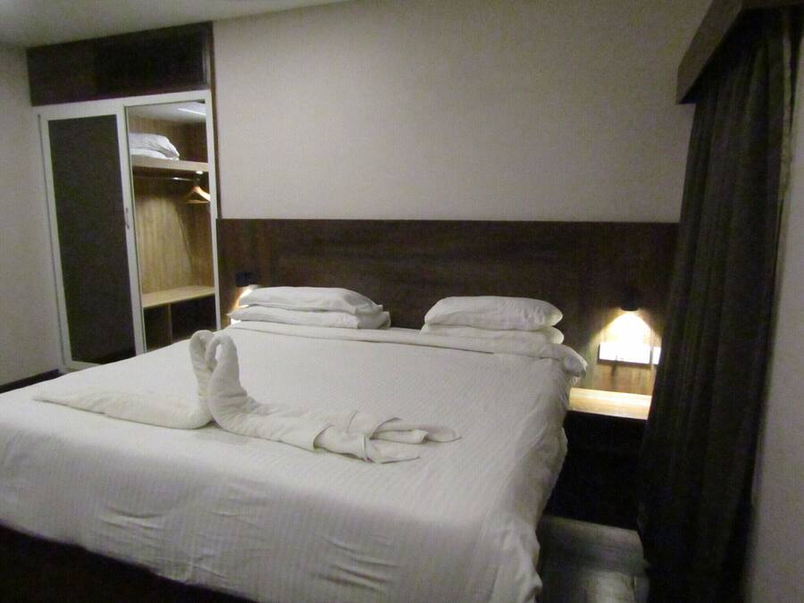A hotel room with a neatly made bed, a wardrobe, and a bedside table with a lamp.