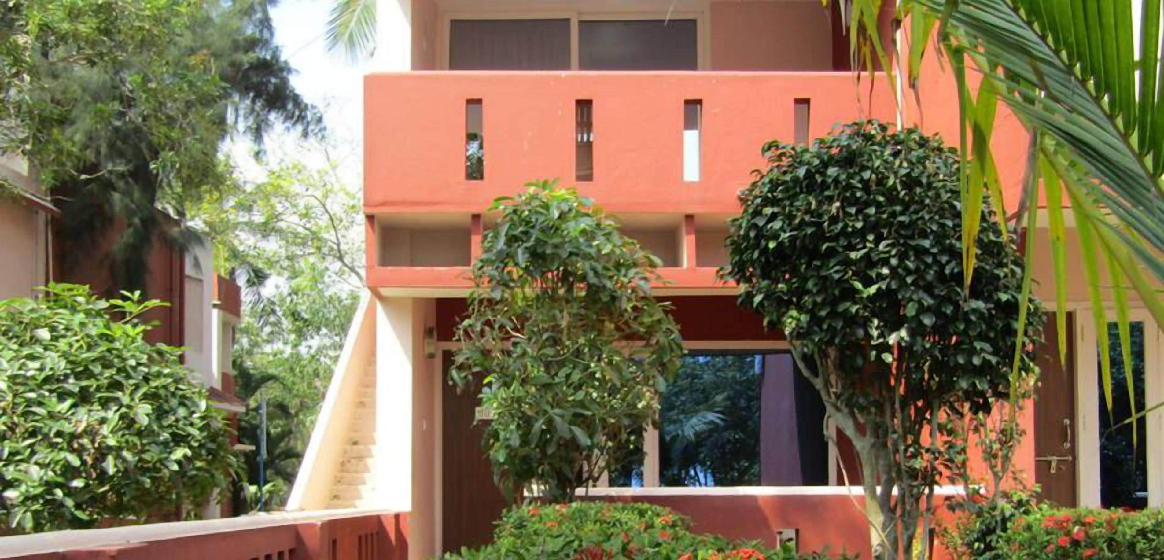 A building with a red facade, a central staircase, and surrounding greenery.