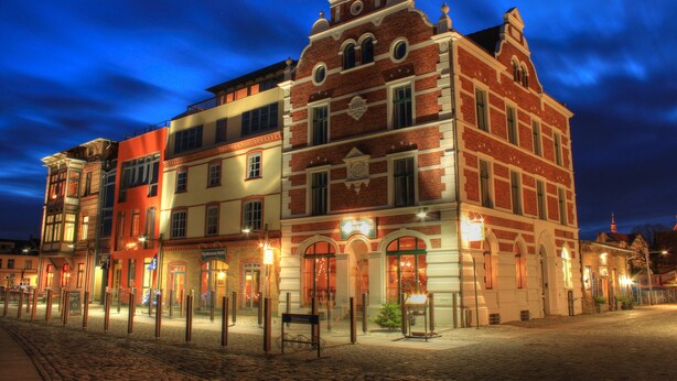 A historic building with a prominent clock tower, arched windows, and a cobblestone street. - Hotel Hiddenseer (Stralsund)
