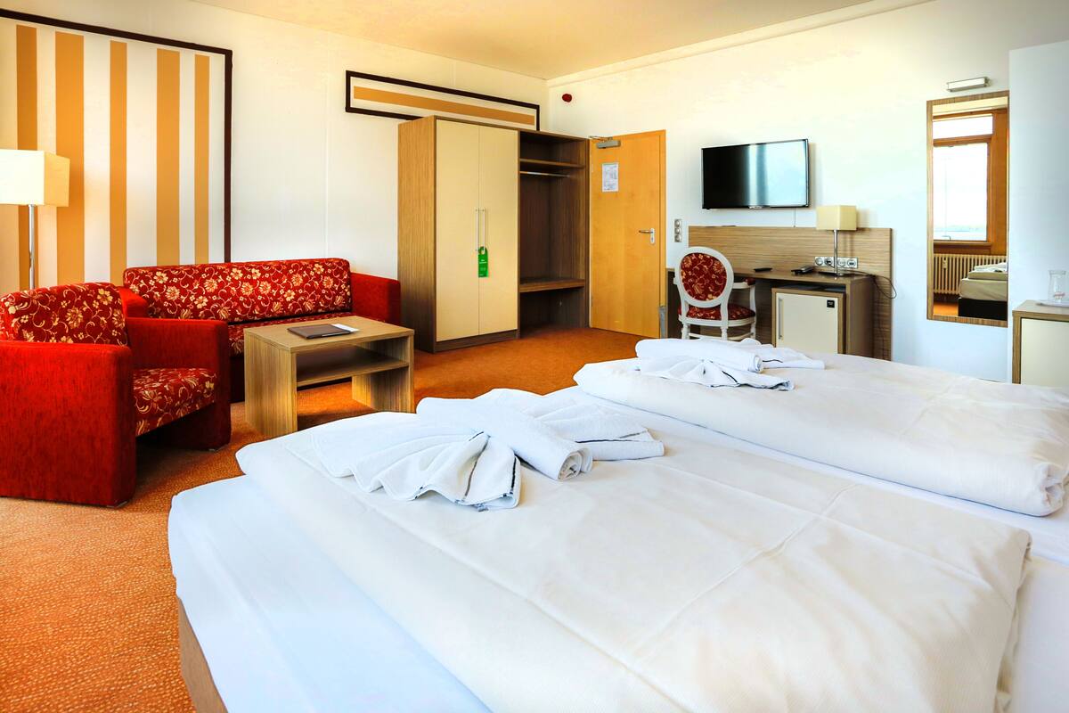 Habitación de hotel con dos camas, un sofá, un escritorio, una silla y un televisor.