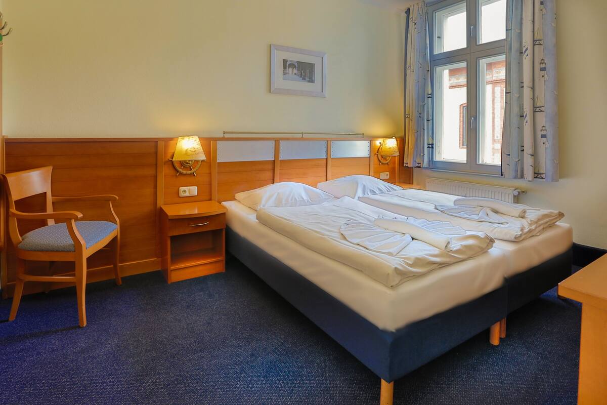 Una habitación de hotel con una cama individual, una silla, una mesita de noche y una ventana con cortinas.