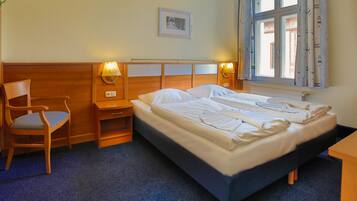 Een hotelkamer met een enkel bed, een stoel, een nachtkastje en een raam met gordijnen.