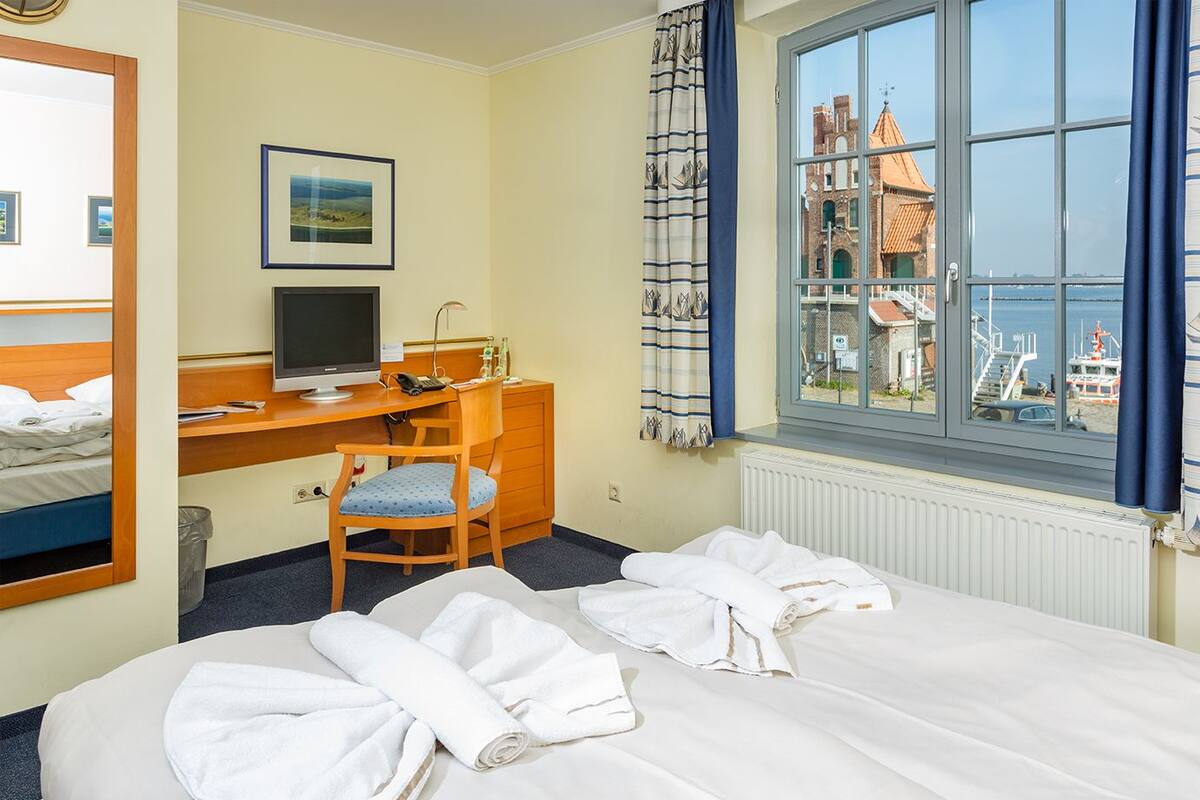 Habitación de hotel con cama, escritorio con computadora, silla y ventana con vista a un edificio y al mar.