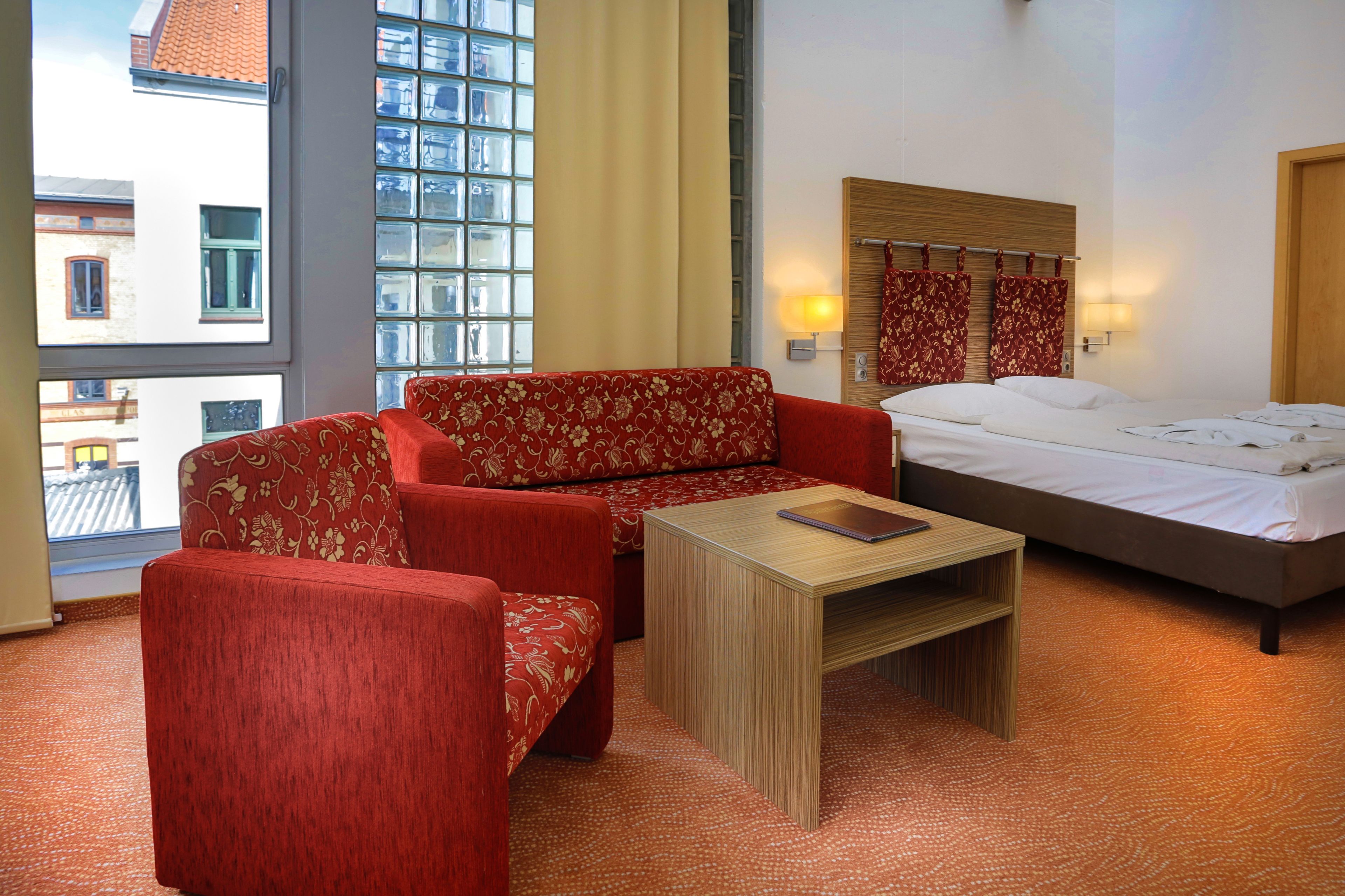 Une chambre d’hôtel avec un lit, un canapé, une petite table et une fenêtre avec des rideaux.