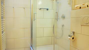 A bathroom with a glass shower enclosure, a toilet, and tiled walls.