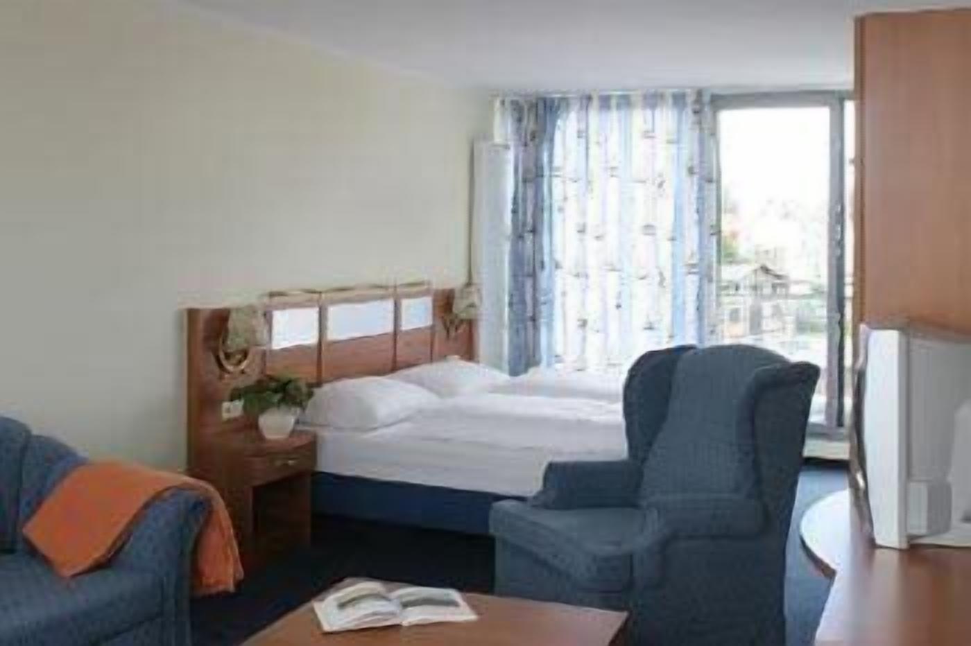 A hotel room with a bed, a chair, a desk, and a window with curtains.