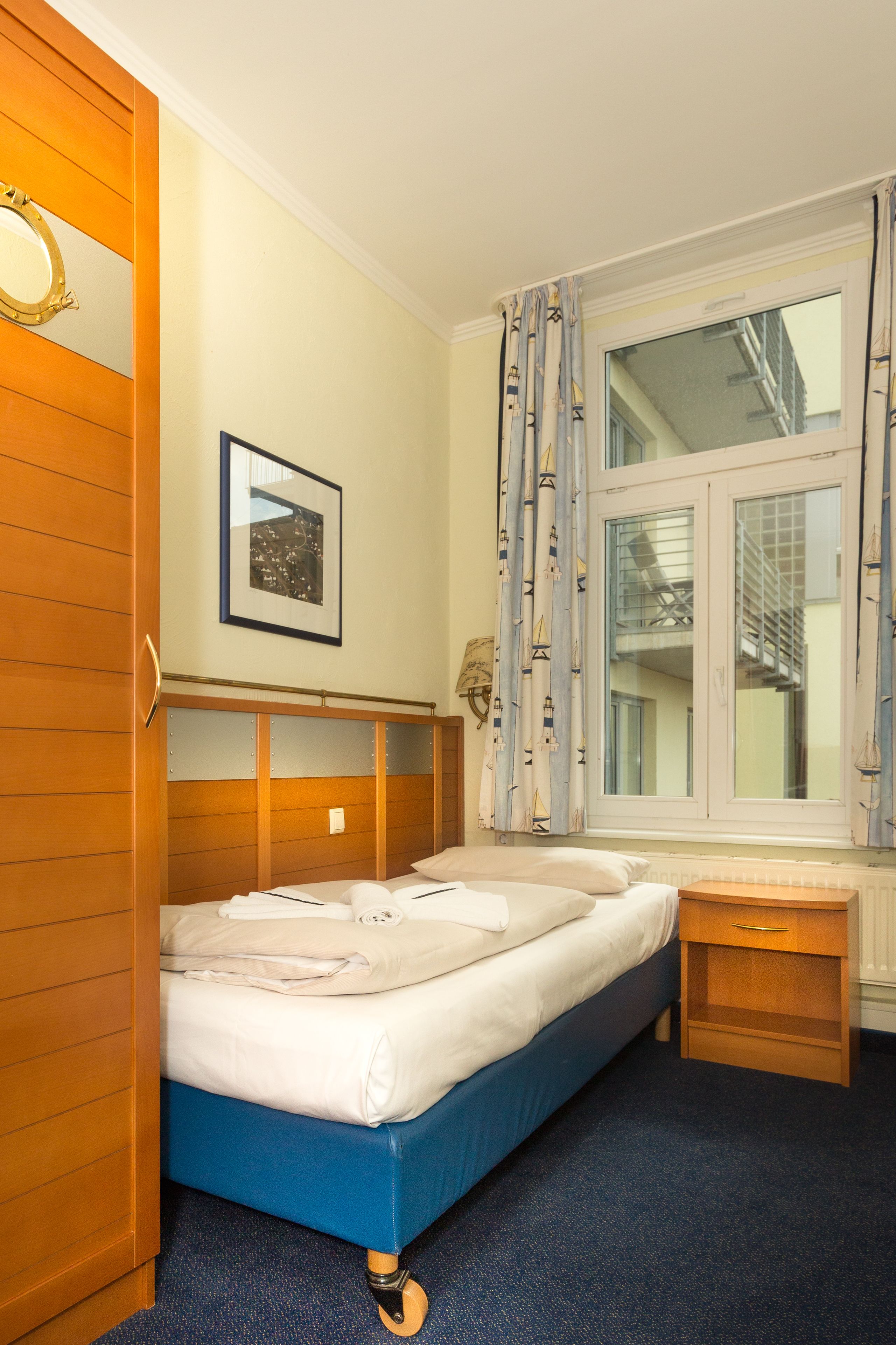 Un dormitorio con cama, armario de madera, mesita de noche, ventana con cortinas e imagen enmarcada en la pared.
