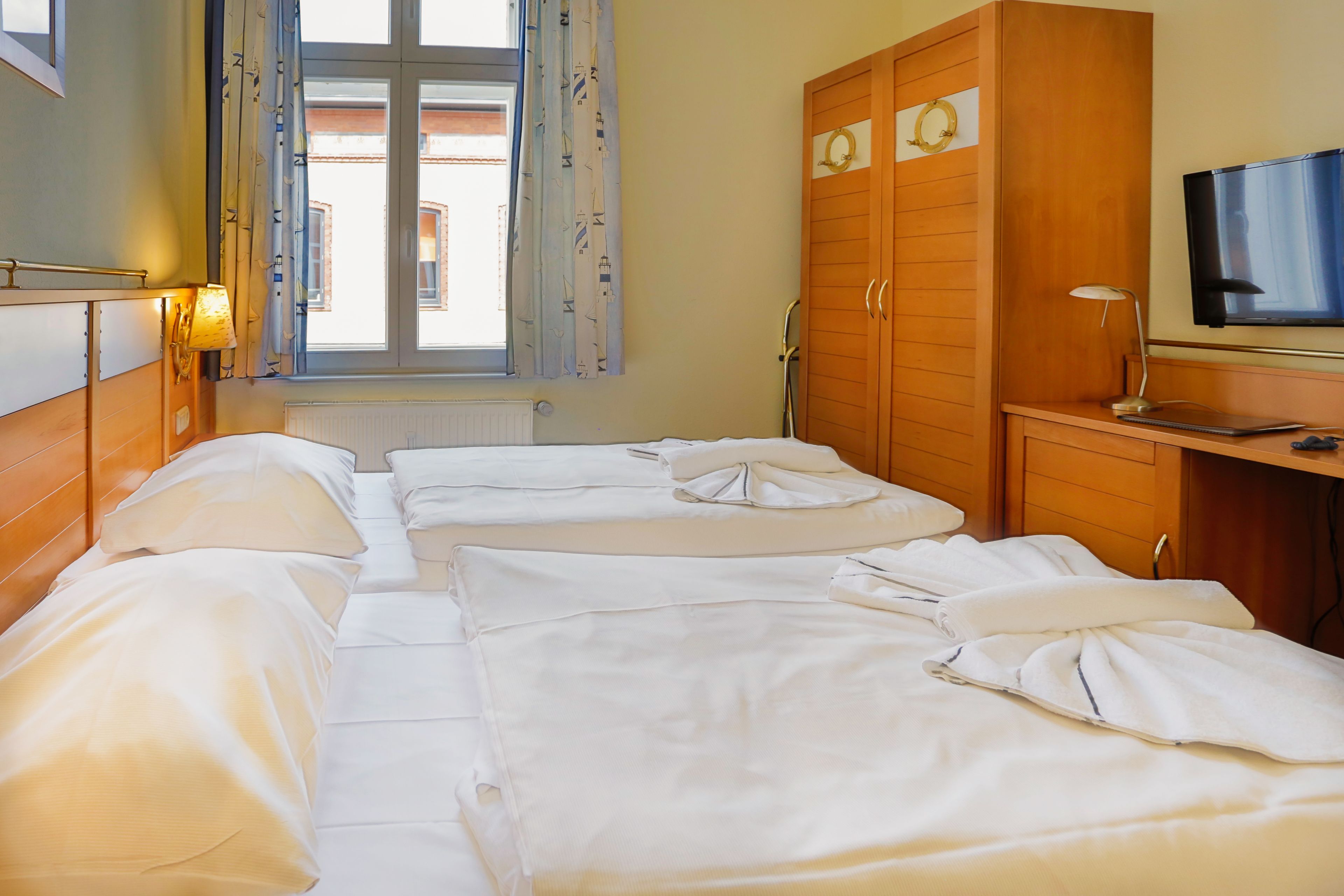Una habitación de hotel con dos camas, televisión, escritorio y ventana con cortinas.
