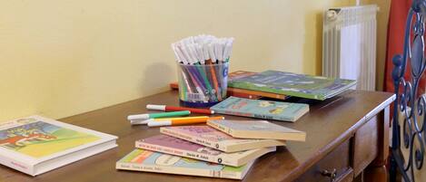 A wooden desk with books, pens, and a cup of markers.