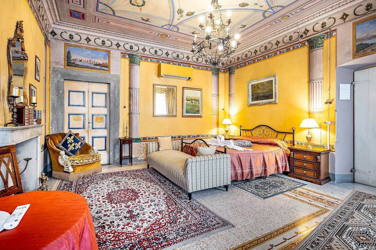 A room with a bed, bedside tables, a chandelier, and a large mirror.