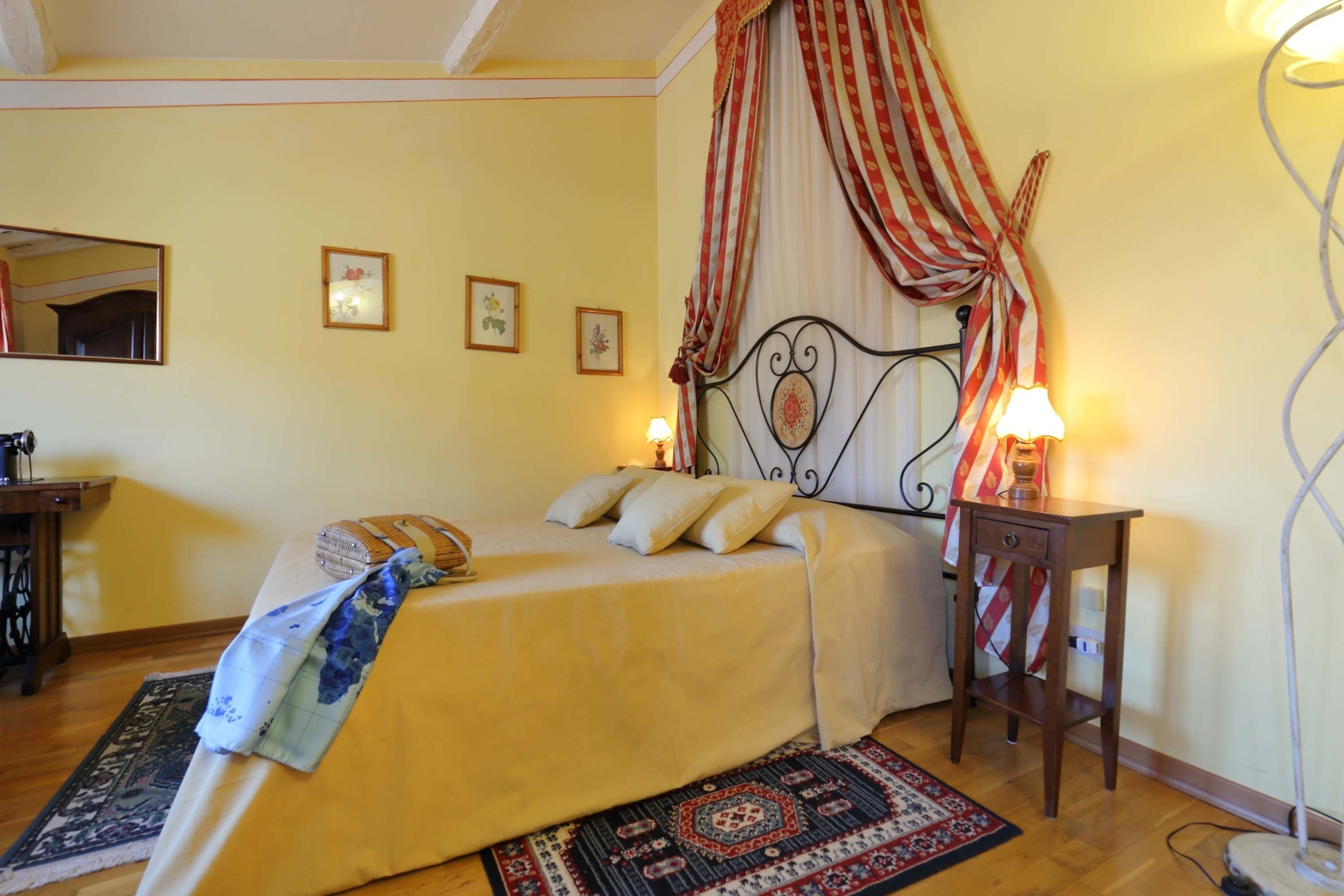 Un dormitorio con cama, mesita de noche, lámpara, espejo y una pared decorada con marcos.