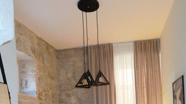 A bedroom with a stone wall, a bed with beige bedding, a hanging light fixture, and a bedside lamp.