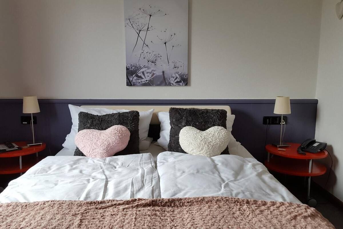 Habitación de hotel ordenada con una cama grande, dos mesitas de noche con lámparas y una obra de arte en la pared.