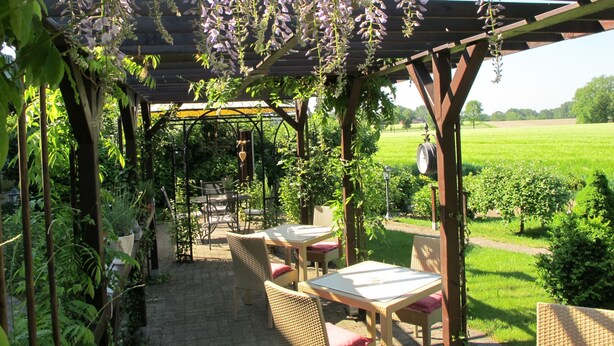 A covered outdoor seating area with wicker furniture and a view of a green field. - Beauty & Wohlfühl Hotel (Syke)