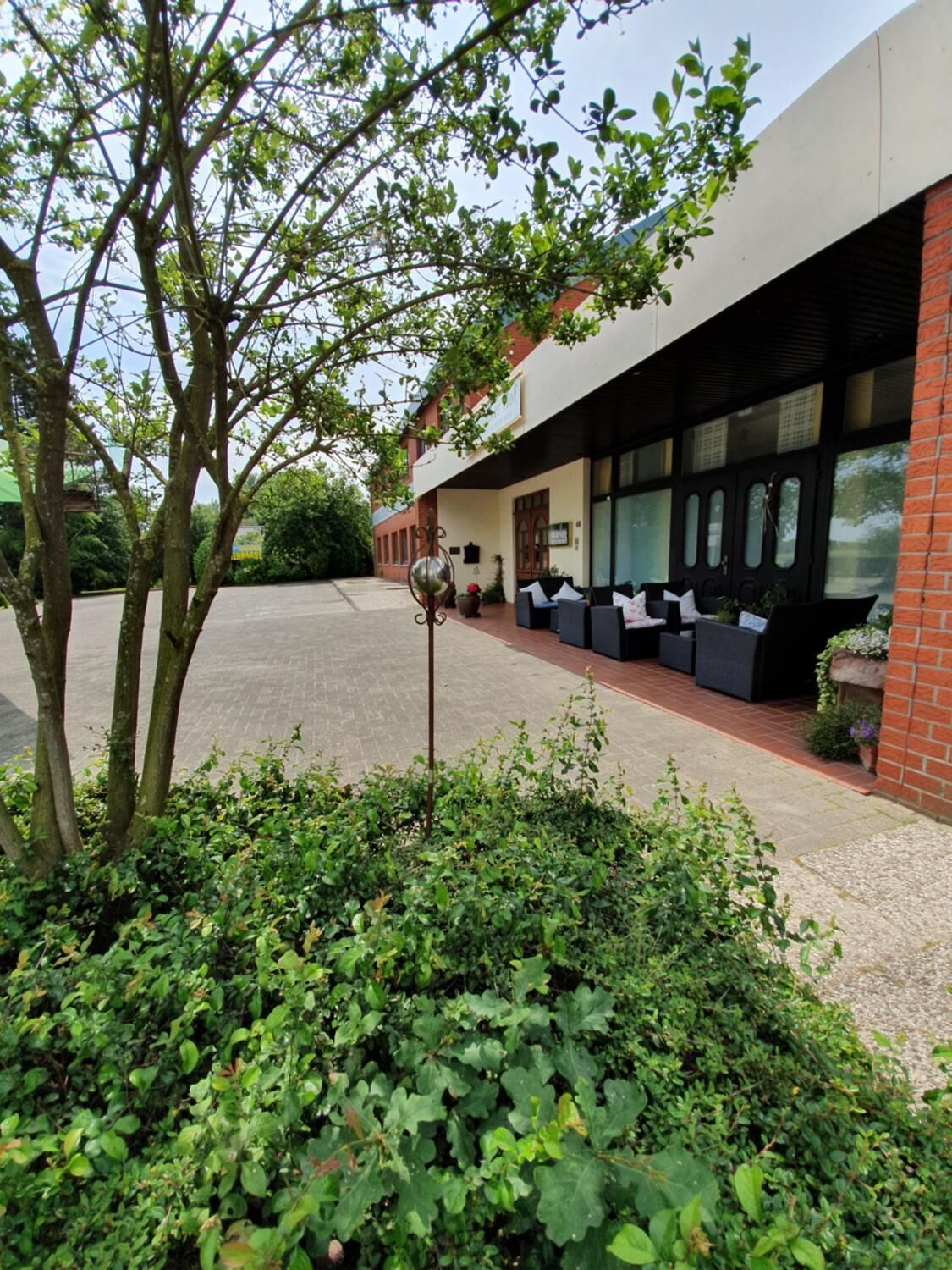 Un edificio con un espacio de estar al aire libre techado, un patio empedrado y un árbol en primer plano.
