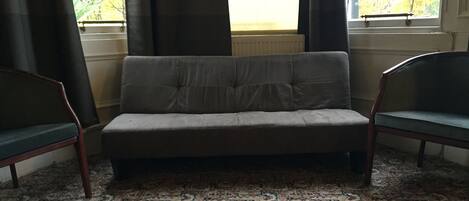 A room with a sofa, two chairs, a patterned carpet, and a window with curtains.