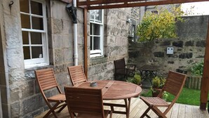 A wooden deck with a round table and four chairs, stone walls, and a hanging plant. - Edinburghhouse Hotel (Edinburgh)