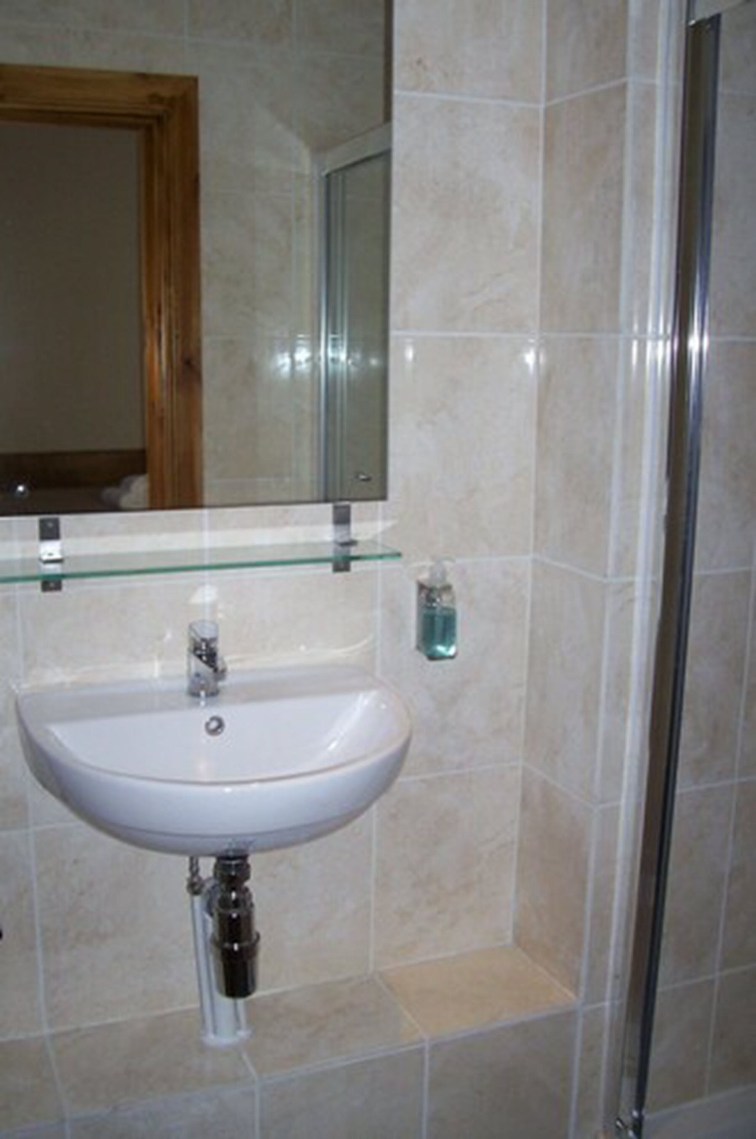 Une salle de bain avec un lavabo blanc, une étagère en verre au-dessus et un miroir.