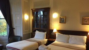 A hotel room with two beds, a wooden cabinet, a chair, and a window with curtains. - Edinburghhouse Hotel (Edinburgh)