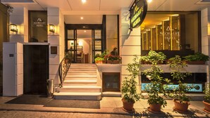 Exterior del Hotel Agorafi con una escalera que lleva a la entrada, plantas en macetas y una fachada bien iluminada.
