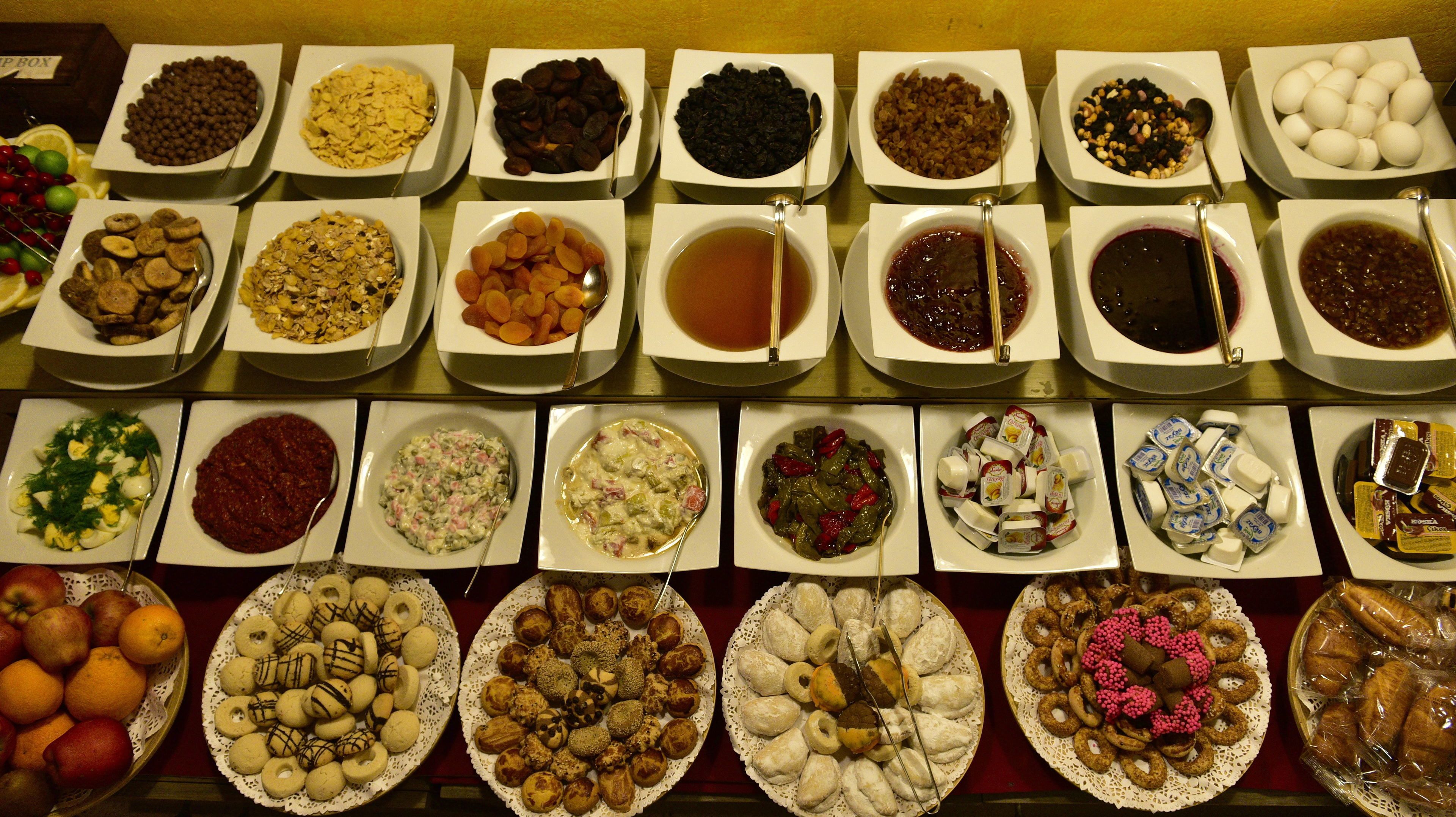 A variety of food items displayed in bowls and plates, including fruits, nuts, and pastries.