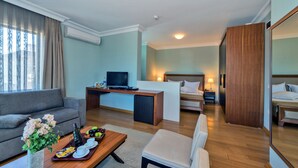 Habitación de hotel con sofá, una mesa de comedor con una bandeja de comida, televisor, escritorio, cama y espejo.