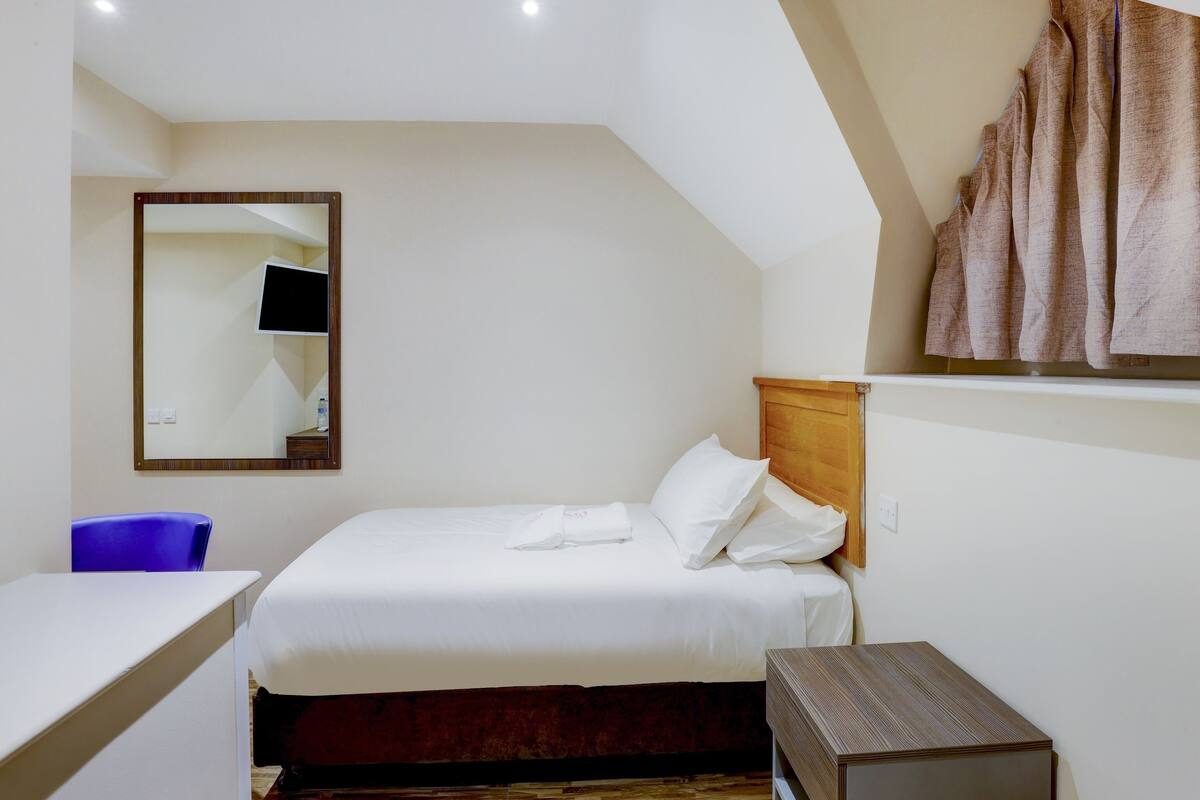 Ett hotellrum med en säng, ett skrivbord, en stol, en spegel och en badrock som hänger på väggen.