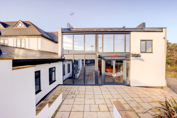 A modern building with a glass entrance, a tiled patio, and a clear sky.