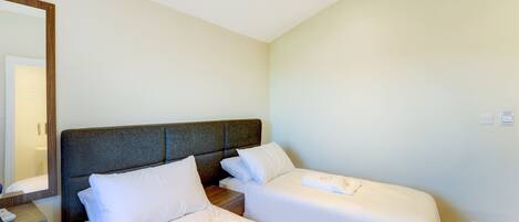 A hotel room with two single beds, a bedside table, a mirror, and a light switch on the wall.