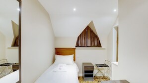 A hotel room with a bed, a wooden headboard, a small table, a chair, a mirror, and a window with a brown curtain.