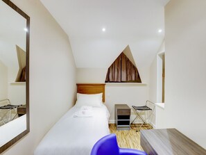 A hotel room with a bed, a wooden headboard, a small table, a chair, a mirror, and a window with a brown curtain.