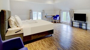 A hotel room with a large bed, a desk, a chair, a TV, and a window.