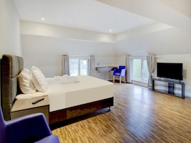 A hotel room with a large bed, a desk, a chair, a TV, and a window.