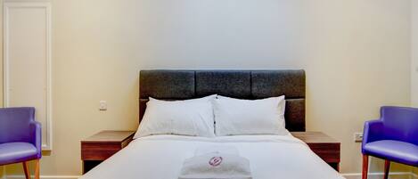Habitación de hotel con cama, dos mesitas de noche, cabecero y dos sillas moradas.