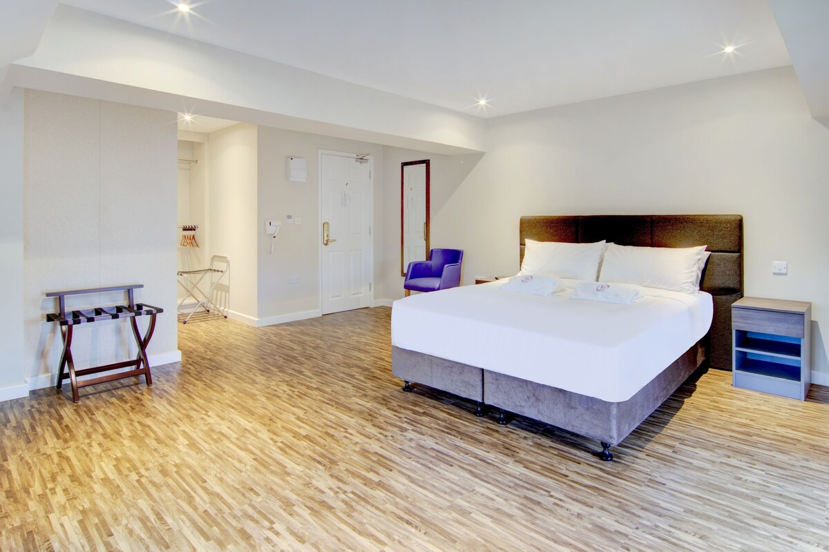 A modern bedroom with a large bed, a wooden floor, a small table, and a chair.