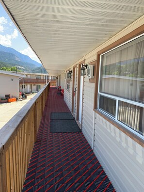 A covered corridor with a red and black patterned floor, wooden railings, and large windows offering a view of a mountainous landscape. - Rondo Motel (Golden)