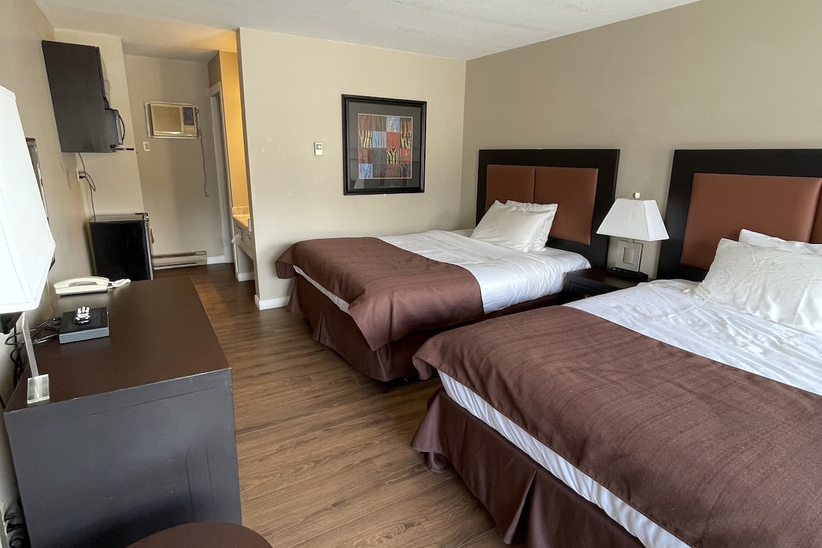 Habitación de hotel con dos camas, un escritorio, una silla, una lámpara y un cuadro en la pared.