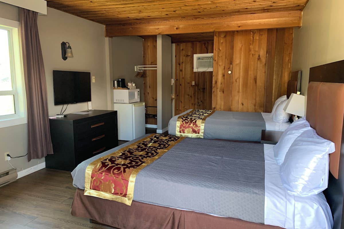 Habitación de hotel con dos camas, televisión, escritorio, microondas y techo de madera.