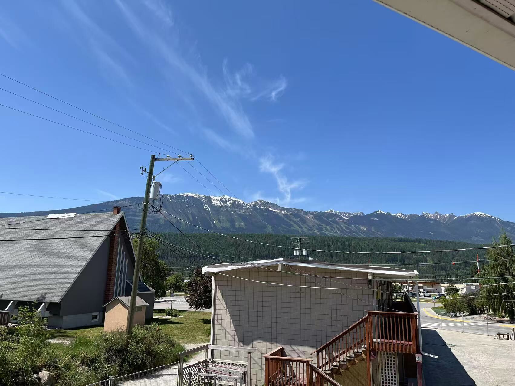 A residential area with a house featuring a sloped roof, a small attached garage, and a staircase leading to a porch. In the background, there are snow-capped mountains and a clear blue sky.